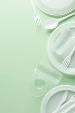 White plastic disposable tableware on green background. Stock Photos
