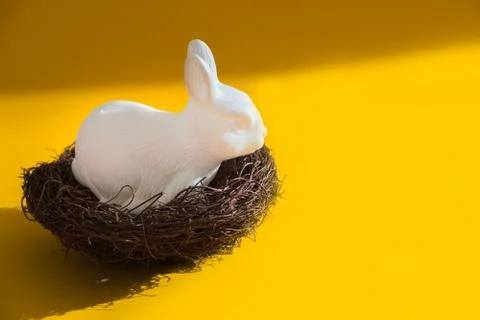 White plastic easter bunny sitting in a nest against a bright yellow backgrou Stock Photos