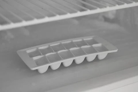 White plastic ice cube tray standing on shelf inside empty refrigerator Stock Photos