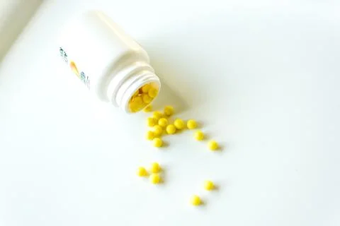 A white plastic jar filled with small yellow dragees lies on its side on a white Stock Photos