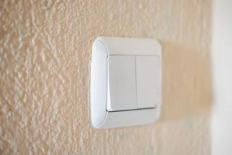 White plastic light switch on a textured beige wall controlling electrical Stock Photos