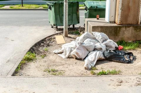 White plastic or nylon garbage bags near plastic dumpster cans full of junk Stock Photos