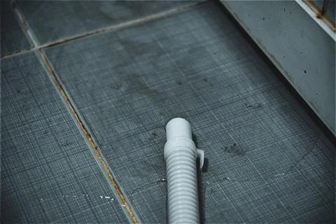 White plastic pipe on a tiled dark floor Stock Photos