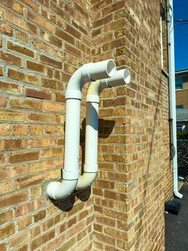 White plastic pipes are fixed to a brown brick wall outside a building on a s Photos