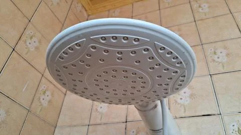 White plastic shower head mounted inside a beige tiled bathroom wall Stock Photos