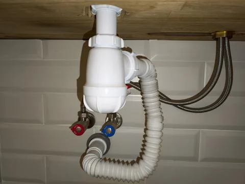 White plastic sink siphon and plumbing under wooden countertop Stock Photos