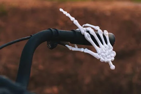 White plastic skeleton hand gripping black rubber handle of vintage bicycle.. Stock Photos