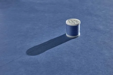 A white plastic spool of sewing thread in a beautiful pale blue color stands  Stock Photos