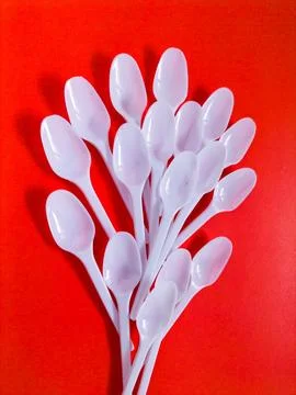 White plastic spoons on red background. Stock Photos