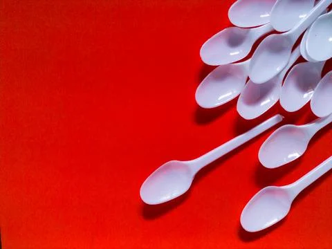White plastic spoons on red background. Stock Photos
