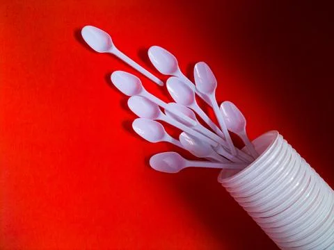 White plastic spoons on red background. Stock Photos