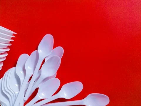 White plastic spoons on red background. Stock Photos