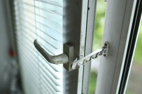 White plastic window frame featuring a metal comb restrictor and handle for Stock Photos