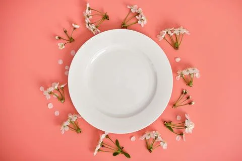 White plate and branches of cherry blossoms on pink background, top view, copy Stock Photos