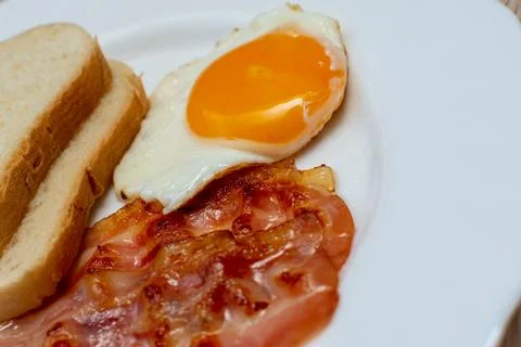 On a white plate bread, chicken egg and fried bacon Stock Photos