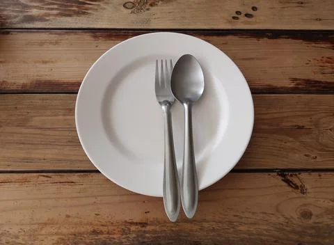 White plate with fork and spoon on wooden table background Stock Photos