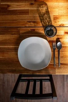 White plate with fork and spoon on wooden table. Sunlit dining place settin.. Stock Photos