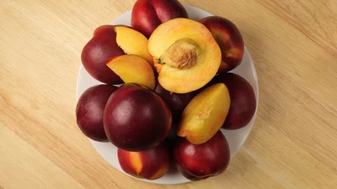 White plate with fresh nectarines rotating on a wooden table Stock Footage 343435516