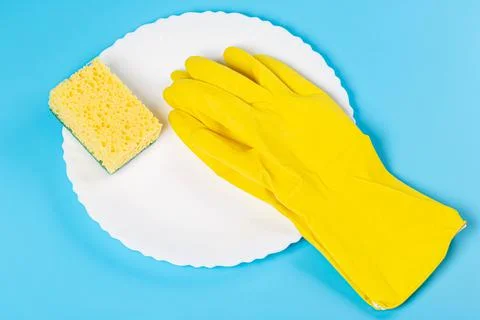 White plate, rubber gloves and a sponge on a blue background Stock Photos