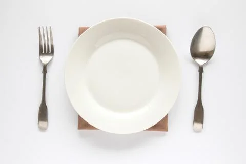 A white plate with silver fork and spoon isolated on white background. Stock Photos