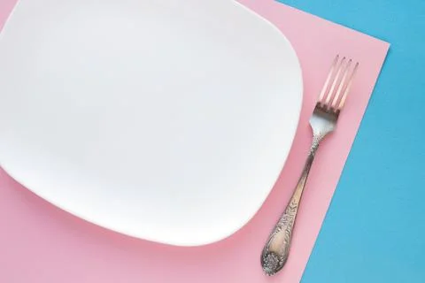 White plate with silver fork on colored background. Top view Stock Photos