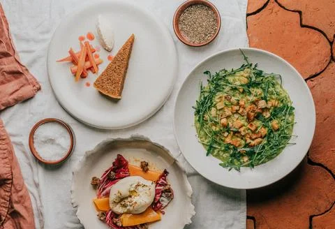 A white plate with a slice of pie sits on a table next to a bowl of greens Stock Photos