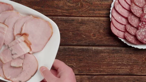 A white plate with sliced ham is placed on a wooden table. Close-up. 库存影片 148344068