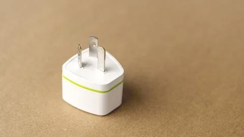 A white plug with a green stripe is located on a brown surface. The plug is.. Stock Photos