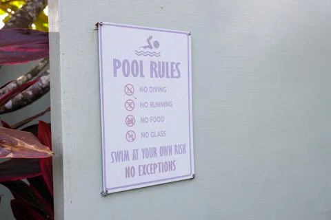 White pool rules sign mounted on a light-colored wall with purple lettering.. Fotos de archivo