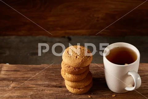 White porcelain mug of tea and sweet cookies on piece of wood over wooden Stock Photos