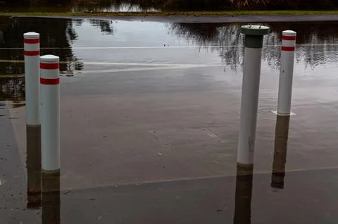 White posts with red reflector tape are surrounded by water in a flooded stre Stock Photos