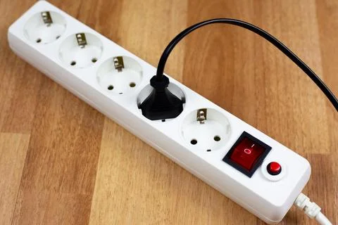 White power strip with red master switch sits on wooden surface. Black appl.. Stock Photos