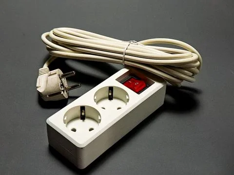 A white power strip with two outlets and coiled cord sits on a gray surface.. Stock Photos