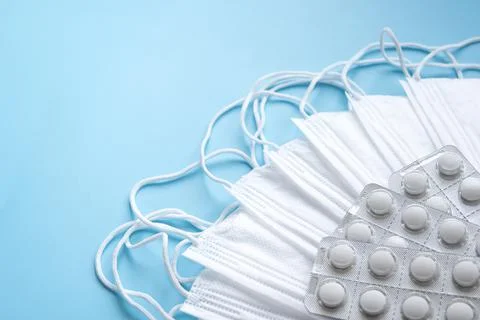 White protective face masks and pills on a blue background Stock Photos