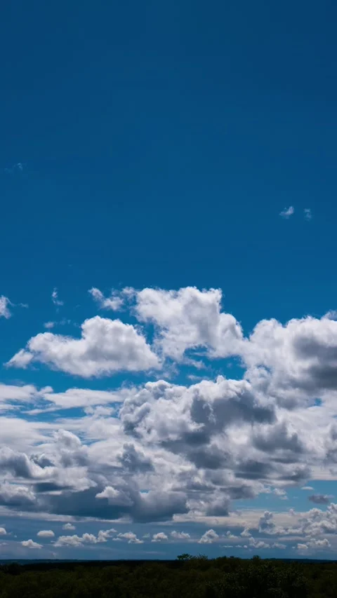 White puffy clouds drift rapidly across a vibrant blue sky in this vertical.. 库存影片 337455207