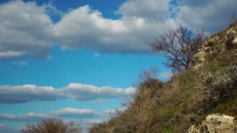 White puffy clouds floating slowly in clear blue sky under wild nature hill on Stock-Footage 107335454