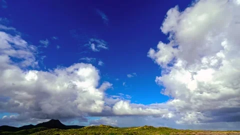 White puffy clouds rolling over rolling green mountain landscape under bright Stock Footage 343695847