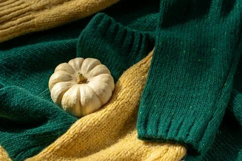White pumpkin near a stack of knitted sweaters on a knitted blanket Stock Photos