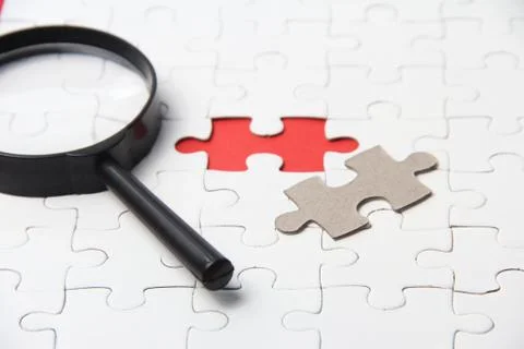 White puzzle with magnifying glass on white background Stock Photos