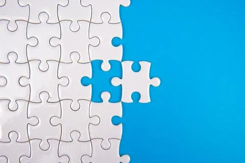 White puzzle with one missing piece on bright blue background. Stock Photos
