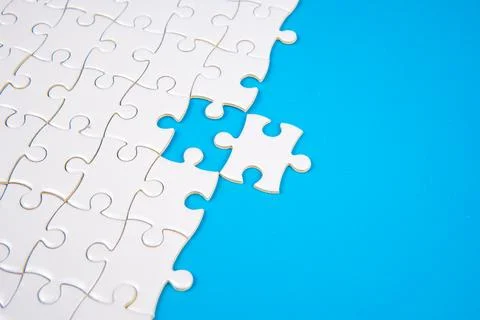 White puzzle with one missing piece on bright blue background. Stock Photos