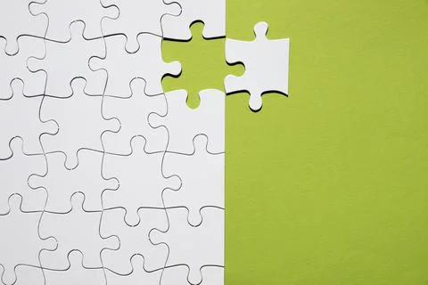 White puzzle piece separate with white puzzle grid green backdrop. High quality Stock Photos