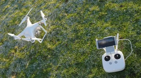 White quadcopter drone with remote controller over a green grass Stock Photos