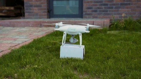 White quadcopter picking up a parcel on ground near the house and flying away to 動画素材 113799006