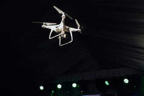 White quadrocopter fly inside the party-tent . Dark background, club light and Stock Photos