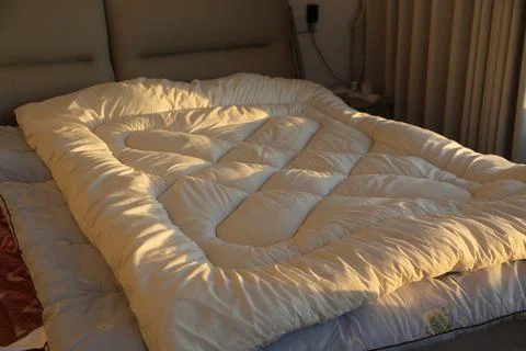 White quilted comforter on a bed in warm sunlight Stock-Fotos