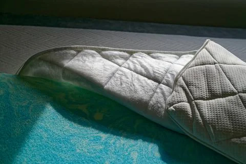 White quilted mattress topper on patterned blue and white bedding in natura.. Stock Photos