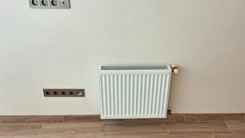 White Radiator with Electrical Outlets on Light Wall and Tiled Floor Stock Footage 331375658