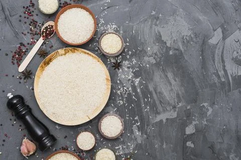 White raw rice with dry spices garlic clove pepper mill concrete backdrop Foto stock