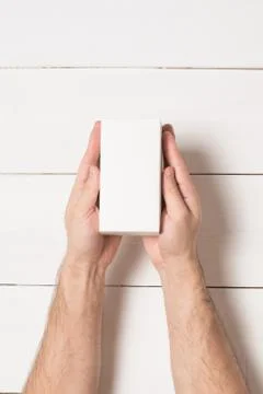 White rectangular box in male hands. Top view. White table on the background 写真素材